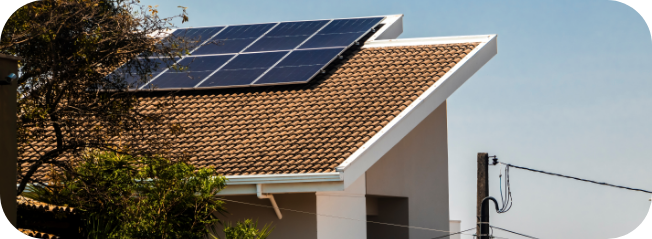 House with rooftop solar panels installed on a tiled roof, with trees and power lines nearby.